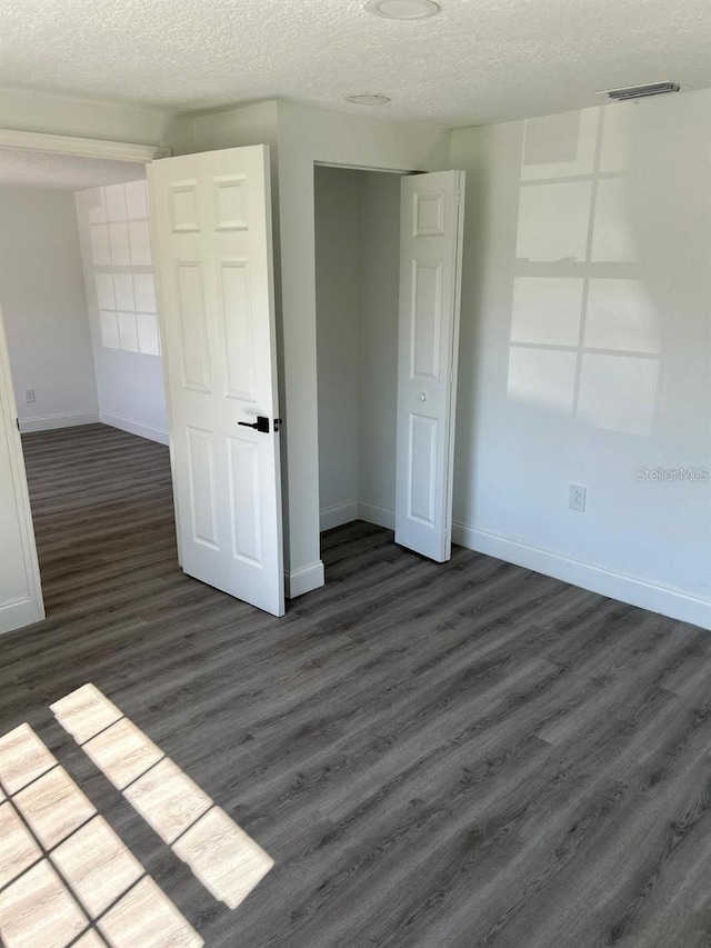 unfurnished bedroom featuring a textured ceiling, dark hardwood / wood-style floors, and a closet