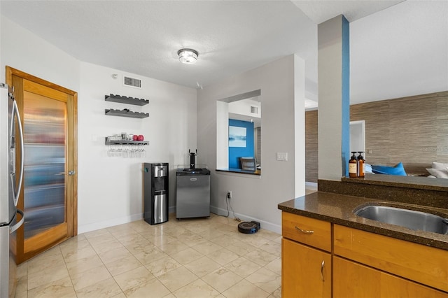 kitchen with stainless steel refrigerator with ice dispenser, a textured ceiling, sink, dark stone countertops, and stainless steel refrigerator