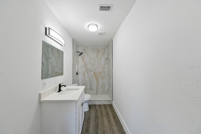 bathroom featuring hardwood / wood-style flooring, vanity, toilet, and a tile shower