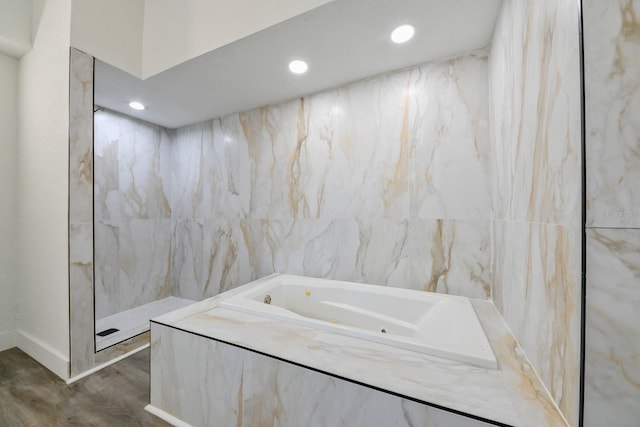 bathroom with tiled tub, tile walls, and hardwood / wood-style flooring