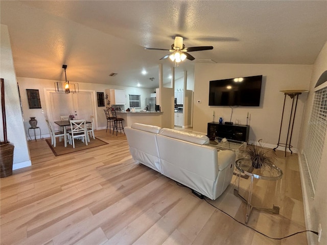 living room featuring a textured ceiling, ceiling fan, light hardwood / wood-style floors, and vaulted ceiling