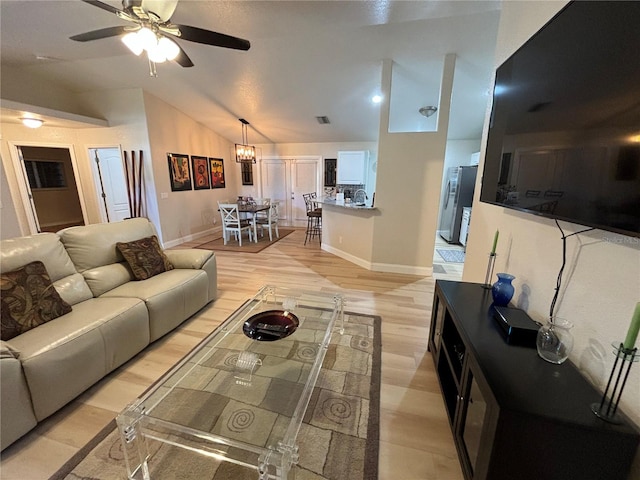 living room with ceiling fan with notable chandelier, light hardwood / wood-style flooring, and vaulted ceiling