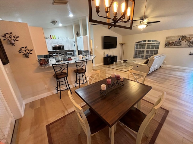 dining space featuring ceiling fan with notable chandelier, light hardwood / wood-style flooring, and vaulted ceiling