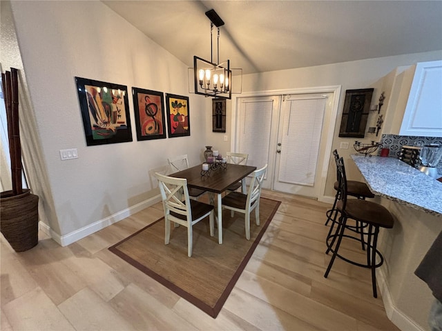 dining area with light hardwood / wood-style floors, vaulted ceiling, and a notable chandelier