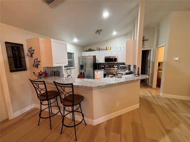 kitchen featuring kitchen peninsula, appliances with stainless steel finishes, light wood-type flooring, tasteful backsplash, and a breakfast bar