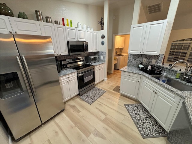 kitchen featuring light stone countertops, sink, decorative backsplash, white cabinets, and appliances with stainless steel finishes