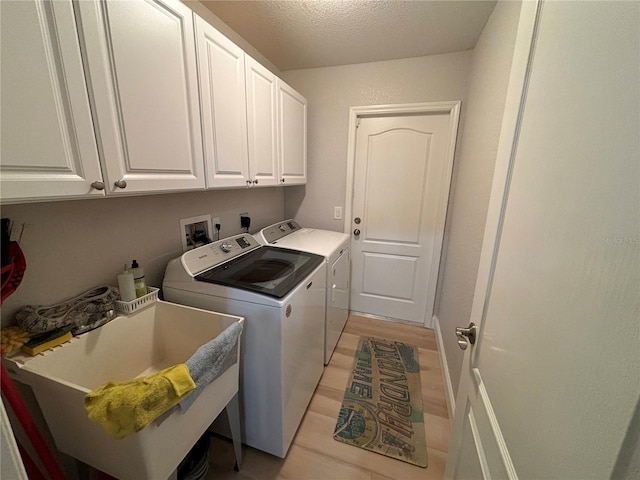 laundry room with washing machine and clothes dryer, sink, cabinets, a textured ceiling, and light wood-type flooring