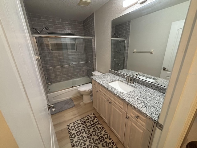 full bathroom featuring combined bath / shower with glass door, vanity, a textured ceiling, wood-type flooring, and toilet