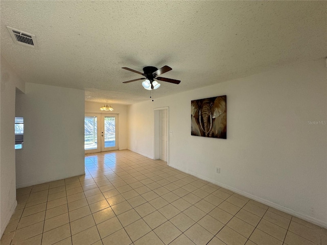 empty room featuring ceiling fan with notable chandelier, french doors, light tile patterned floors, and a textured ceiling