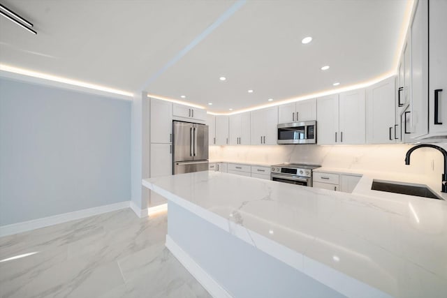 kitchen with white cabinets, sink, light stone countertops, kitchen peninsula, and stainless steel appliances