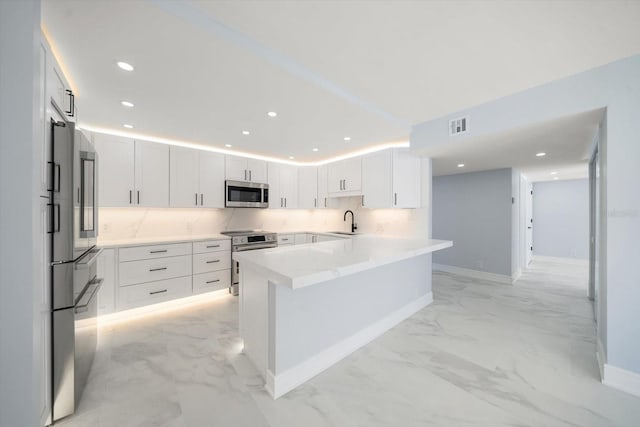 kitchen with sink, stainless steel appliances, a barn door, backsplash, and white cabinets