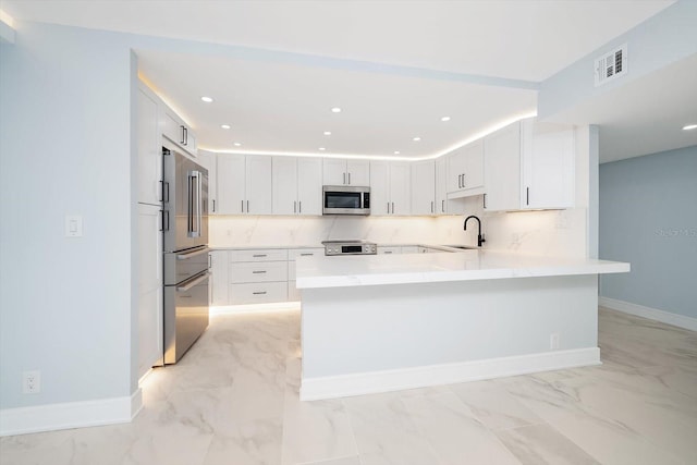 kitchen with appliances with stainless steel finishes, light marble finish flooring, a peninsula, a sink, and baseboards
