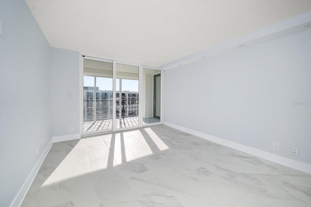 unfurnished room featuring expansive windows, marble look tile flooring, and baseboards