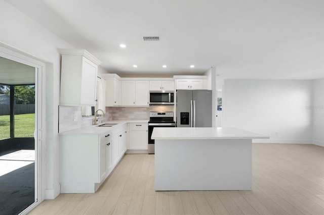 kitchen with white cabinetry, sink, a center island, appliances with stainless steel finishes, and light wood-type flooring