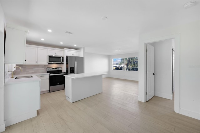 kitchen featuring a center island, sink, appliances with stainless steel finishes, light hardwood / wood-style floors, and white cabinetry