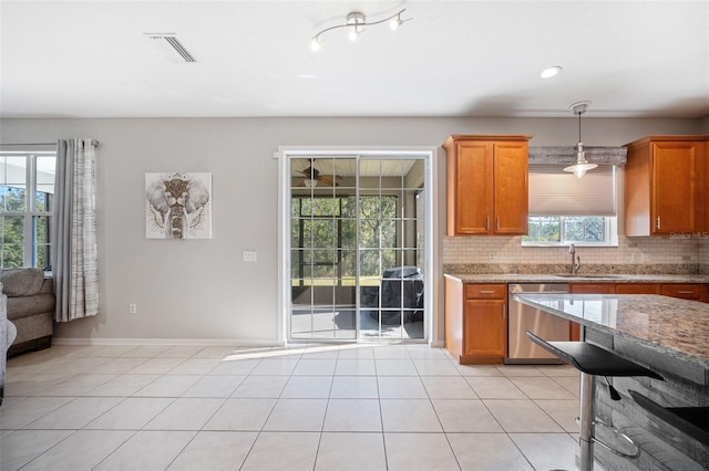 kitchen featuring light stone countertops, dishwasher, sink, decorative light fixtures, and decorative backsplash