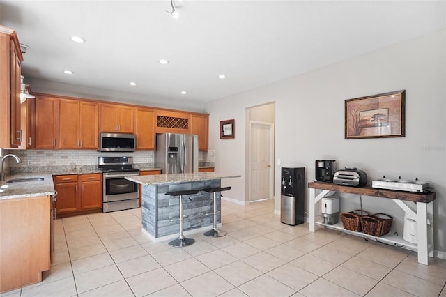 kitchen featuring a center island, sink, stainless steel appliances, light stone counters, and a breakfast bar area