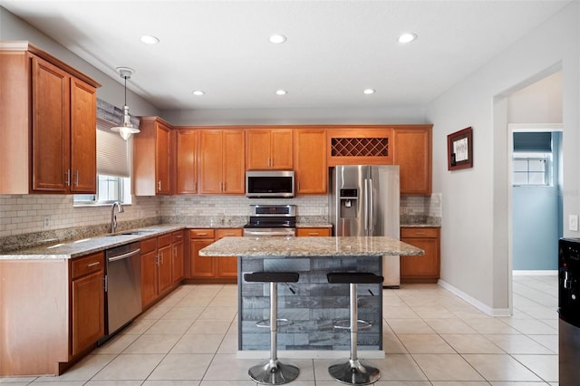 kitchen with light stone counters, stainless steel appliances, sink, a kitchen island, and hanging light fixtures