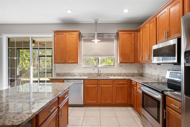 kitchen featuring sink, light tile patterned floors, light stone countertops, appliances with stainless steel finishes, and decorative light fixtures