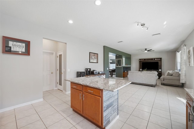 kitchen with a center island, light stone counters, ceiling fan, and light tile patterned flooring