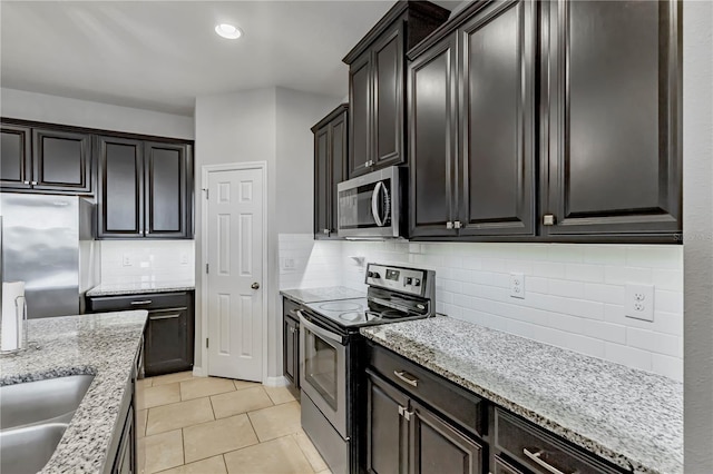 kitchen featuring light stone countertops, stainless steel appliances, light tile patterned floors, backsplash, and sink