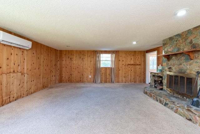 unfurnished living room with a textured ceiling, wooden walls, an AC wall unit, carpet floors, and a stone fireplace