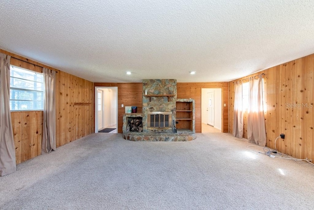 unfurnished living room with carpet flooring, a fireplace, wooden walls, and a textured ceiling