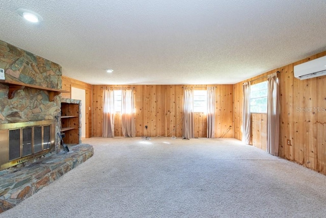 unfurnished living room with carpet flooring, a stone fireplace, wooden walls, and a textured ceiling