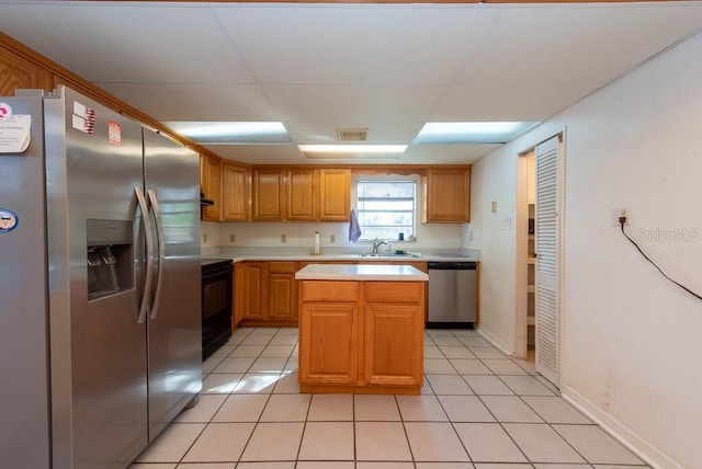 kitchen with appliances with stainless steel finishes, sink, a kitchen island, and light tile patterned flooring