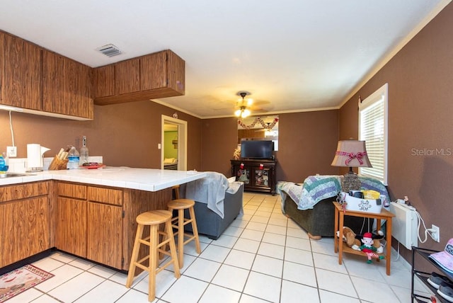 kitchen featuring tile countertops, crown molding, ceiling fan, kitchen peninsula, and a breakfast bar area