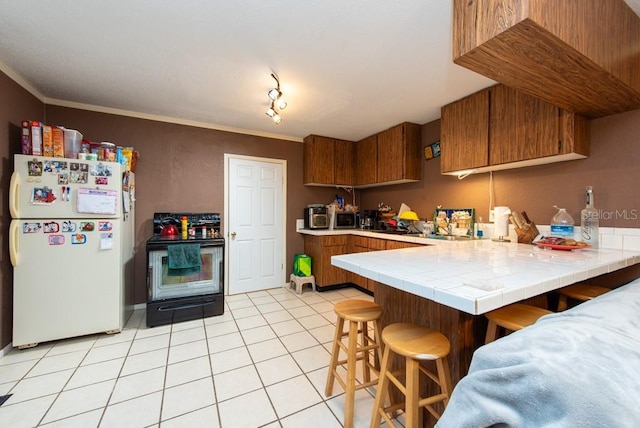 kitchen featuring kitchen peninsula, crown molding, tile countertops, white fridge, and a breakfast bar