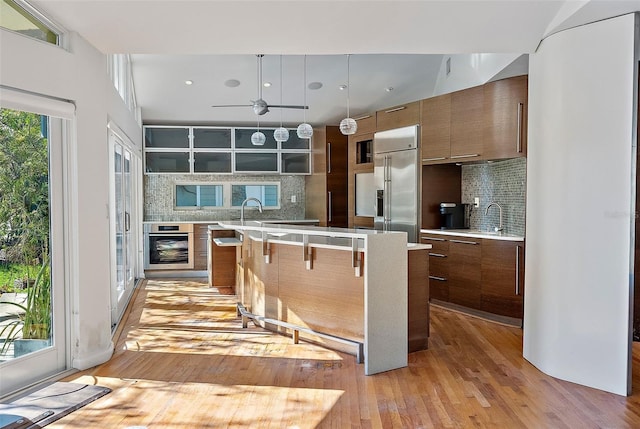 kitchen with tasteful backsplash, built in refrigerator, hanging light fixtures, and light hardwood / wood-style floors