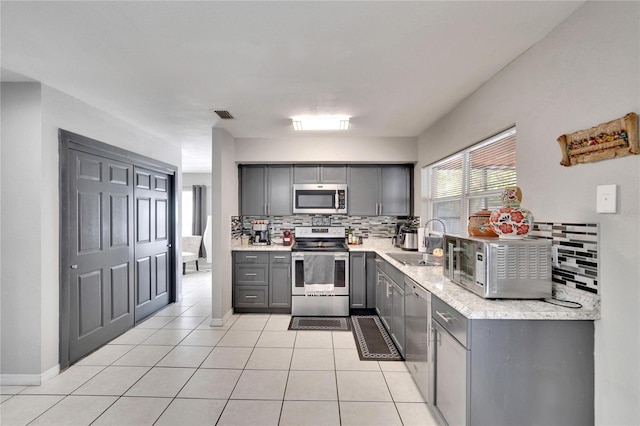 kitchen with backsplash, sink, gray cabinets, light tile patterned floors, and appliances with stainless steel finishes