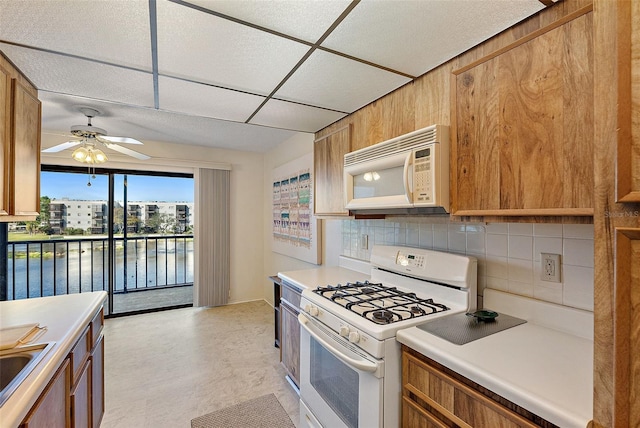 kitchen with decorative backsplash, white appliances, ceiling fan, sink, and a water view