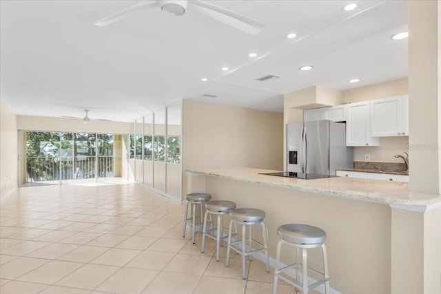 kitchen with light stone countertops, black electric stovetop, a kitchen breakfast bar, white cabinets, and stainless steel fridge with ice dispenser