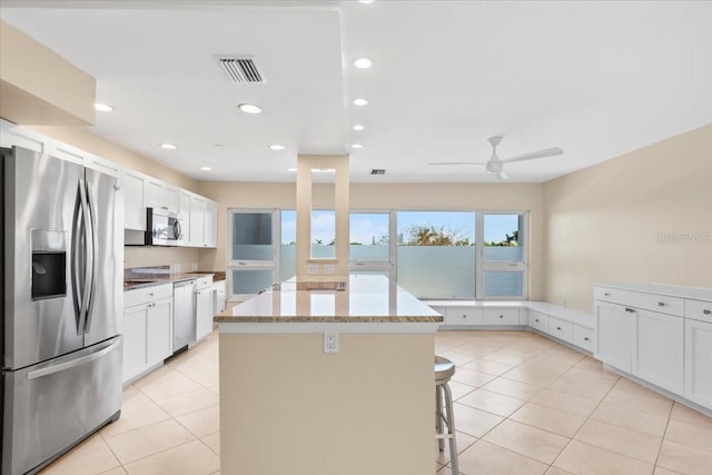 kitchen with light stone countertops, appliances with stainless steel finishes, a kitchen breakfast bar, white cabinets, and a kitchen island