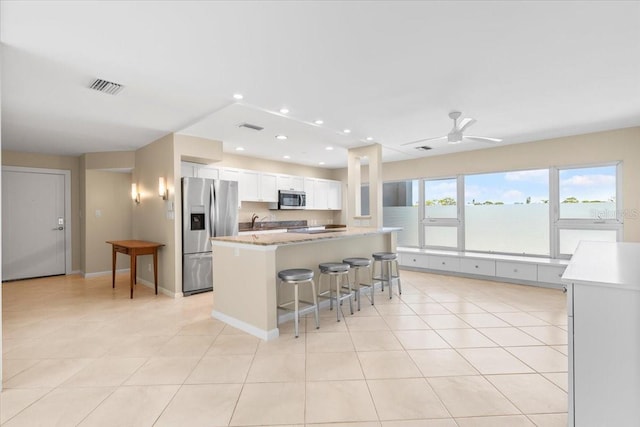 kitchen featuring appliances with stainless steel finishes, a kitchen breakfast bar, ceiling fan, white cabinetry, and light tile patterned flooring