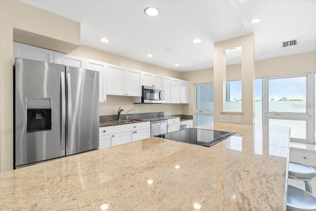 kitchen featuring white cabinets, stainless steel appliances, light stone counters, and sink