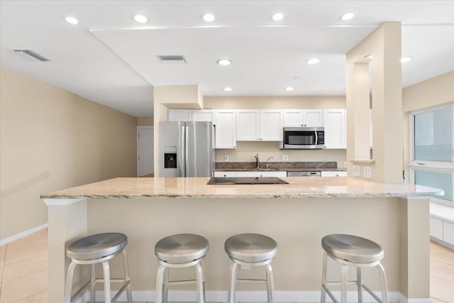 kitchen with light stone countertops, a kitchen breakfast bar, stainless steel appliances, light tile patterned floors, and white cabinets