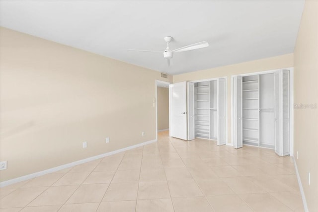 unfurnished bedroom with ceiling fan, light tile patterned flooring, and two closets