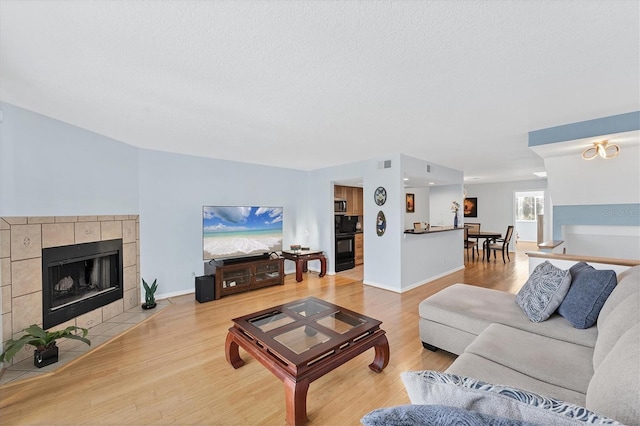 living room featuring light wood-type flooring, a textured ceiling, and a tile fireplace