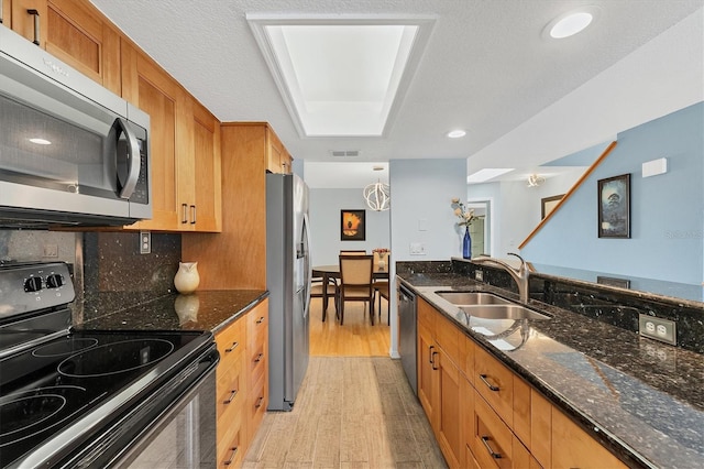 kitchen featuring dark stone countertops, sink, light wood-type flooring, and stainless steel appliances