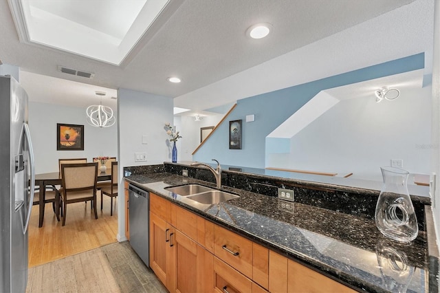 kitchen with appliances with stainless steel finishes, dark stone counters, sink, decorative light fixtures, and light hardwood / wood-style floors