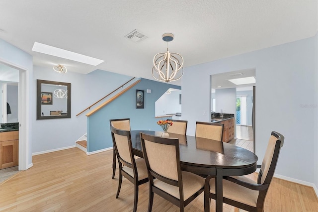 dining space with a notable chandelier, a skylight, a textured ceiling, and light hardwood / wood-style flooring