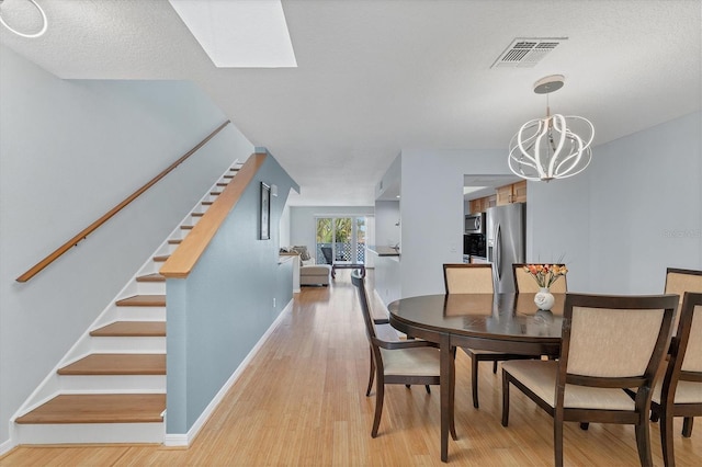 dining room with a textured ceiling, light wood-type flooring, a skylight, and a notable chandelier