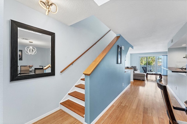 stairway with a chandelier, wood-type flooring, and a textured ceiling