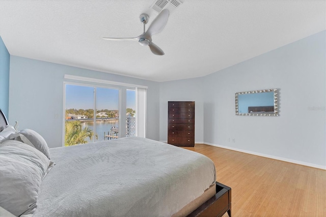 bedroom with a textured ceiling, access to outside, ceiling fan, a water view, and hardwood / wood-style floors