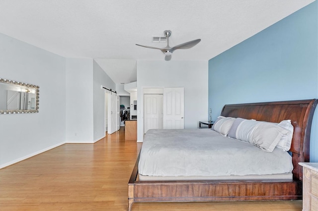 bedroom with ceiling fan, a barn door, hardwood / wood-style floors, vaulted ceiling, and a textured ceiling