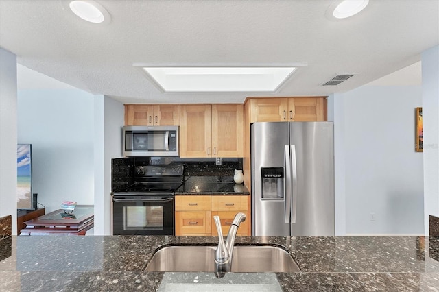 kitchen with backsplash, sink, a skylight, dark stone countertops, and stainless steel appliances