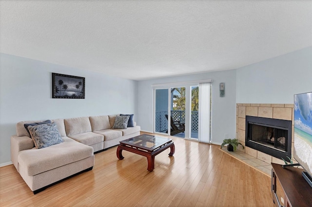 living room with a textured ceiling, light wood-type flooring, and a tiled fireplace